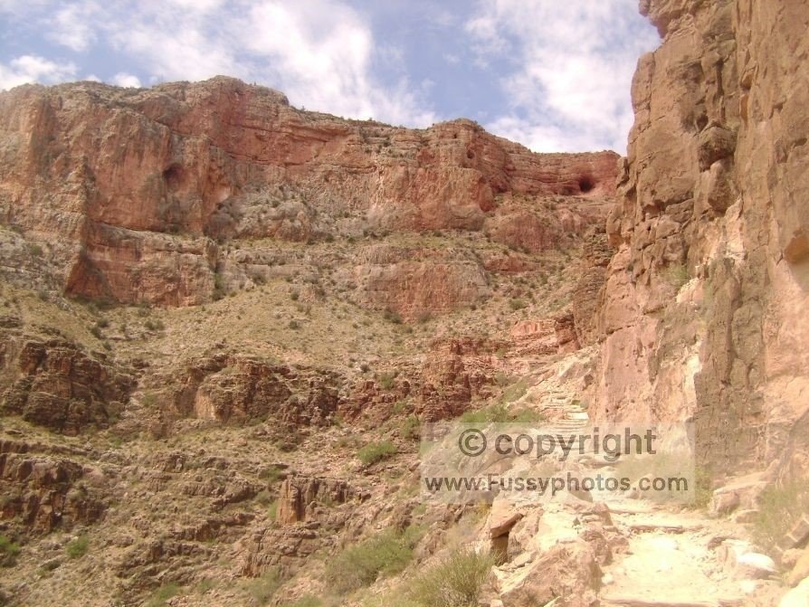 A steep, exposed section of the South Kaibab Trail rising through sunlit canyon layers with no shade.