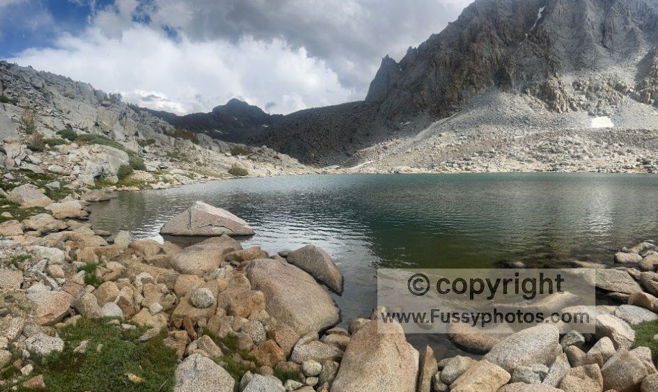 Eastward view in Darwin Canyon with a small lake in the foreground and scattered boulders, representing one of the easier navigation sections on the route to Lamarck Col.