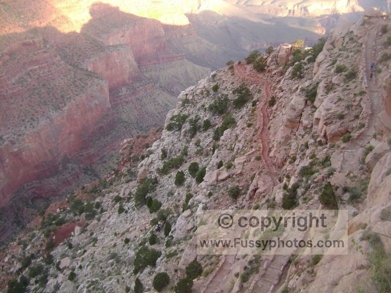 A view of the South Kaibab Trail’s tight switchbacks descending through exposed canyon rock layers, with hikers making their way down the steep, open terrain.