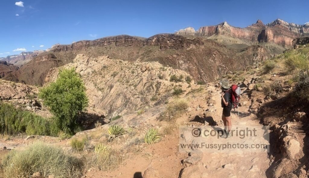 Hikers ascending the Bright Angel Trail beneath layered canyon walls on a steep, exposed section of the climb.