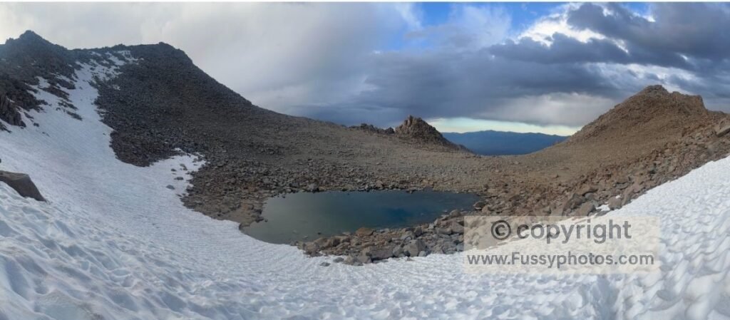 Eastward view just beyond Lamarck Col, showing a narrow rock gap, a cirque tarn, and a steep snowfield covering the pass’s north face.