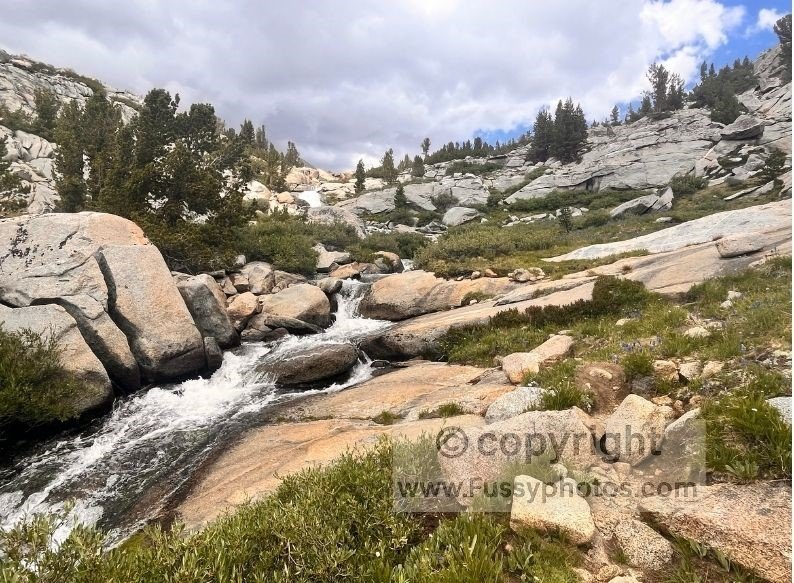 Steep, rugged terrain with cascading waterfalls and scattered boulders as the route climbs north toward Darwin Bench, with The Hermit visible above.