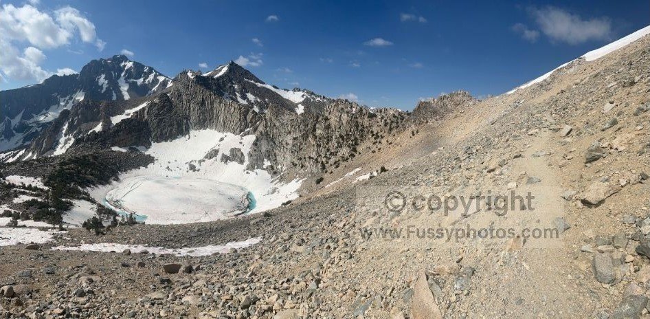 Frozen Big Pothole Lake just below Kearsarge Pass, surrounded by rugged granite peaks and high‑alpine terrain in midsummer.