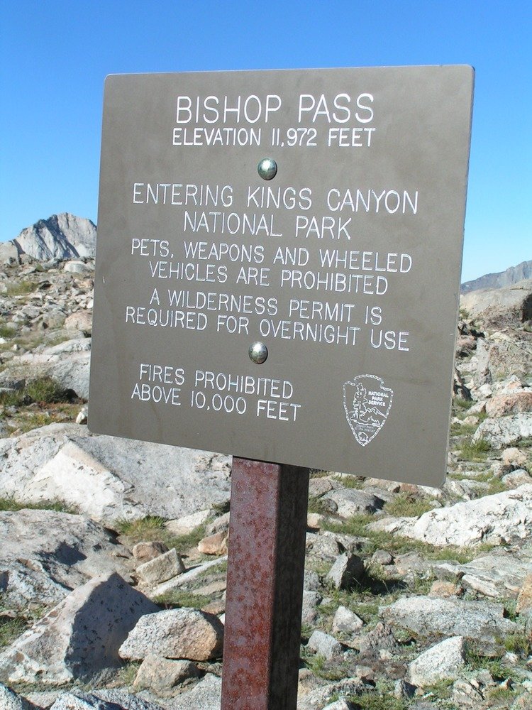Elevation sign at Bishop Pass set against high‑alpine granite peaks and open terrain, marking one of the easier east‑side approaches to the John Muir Trail.