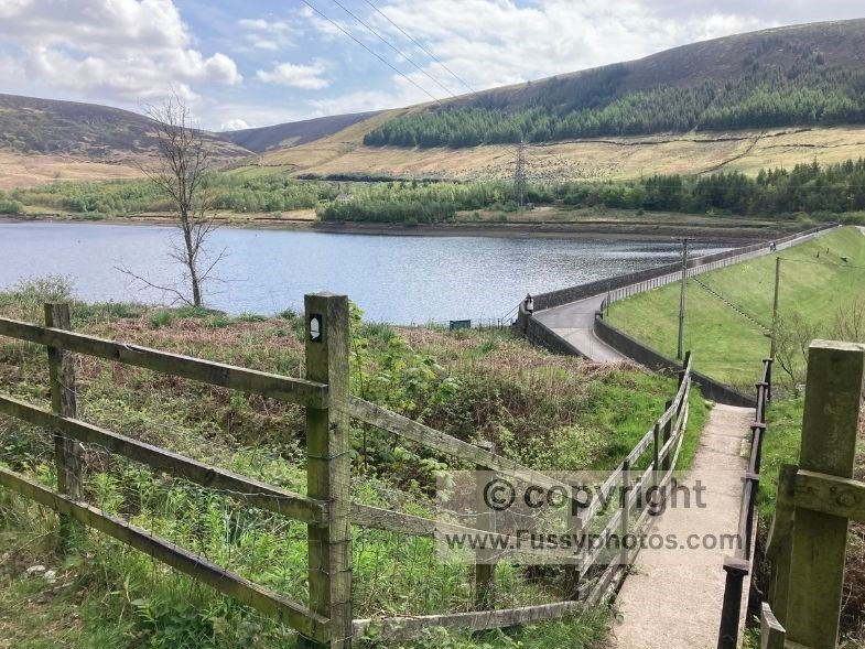 Walker crossing Torside Reservoir on the Pennine Way near Crowden, with Dark Peak moorland rising ahead at the end of Day 1.