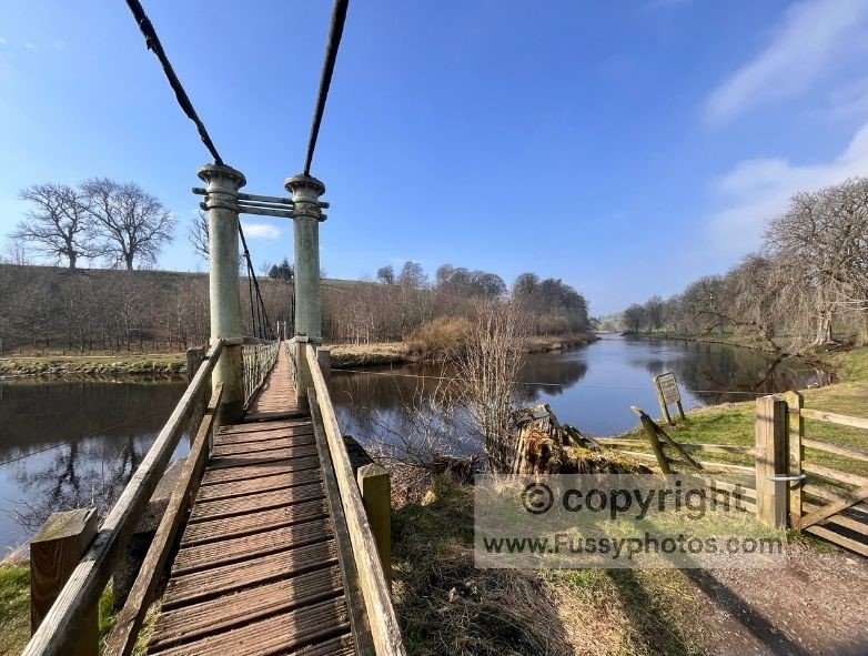 Walker crossing Hebden Suspension Bridge from the north bank to the south on the Dales Way near Grassington.