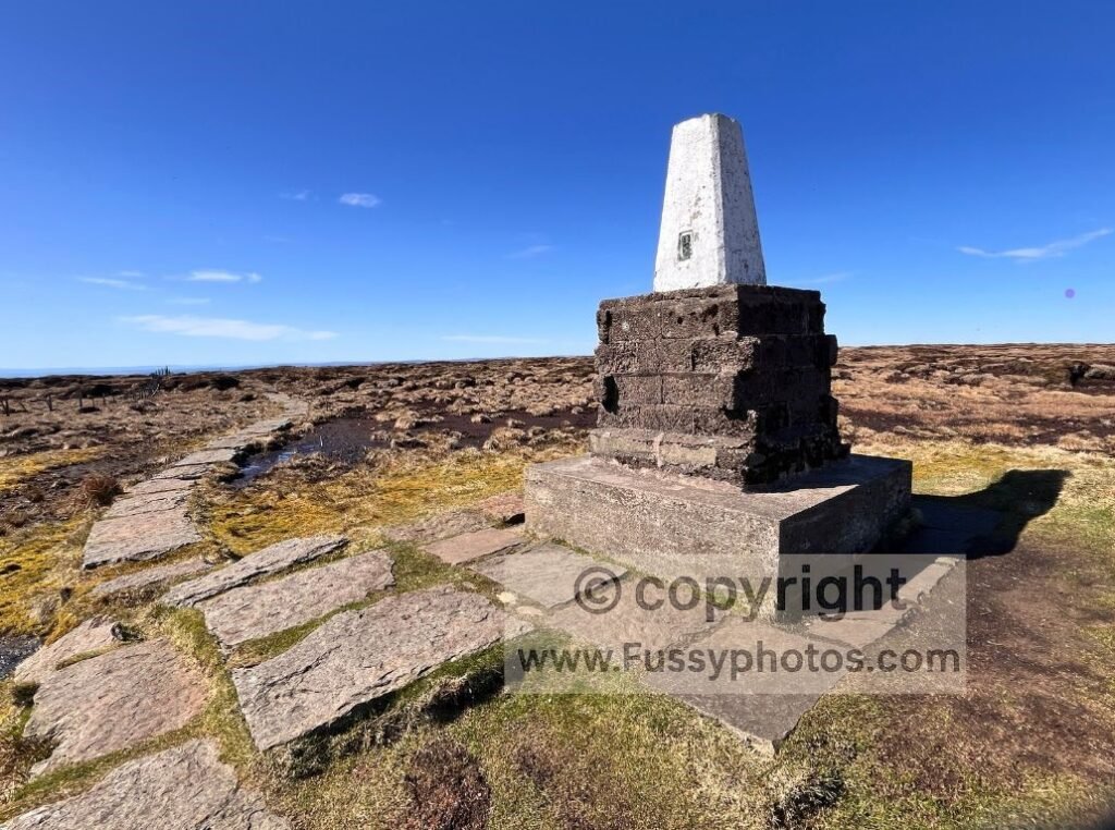 Southwest‑facing view from the flat, boggy summit of The Cheviot, with the trig point in the foreground.