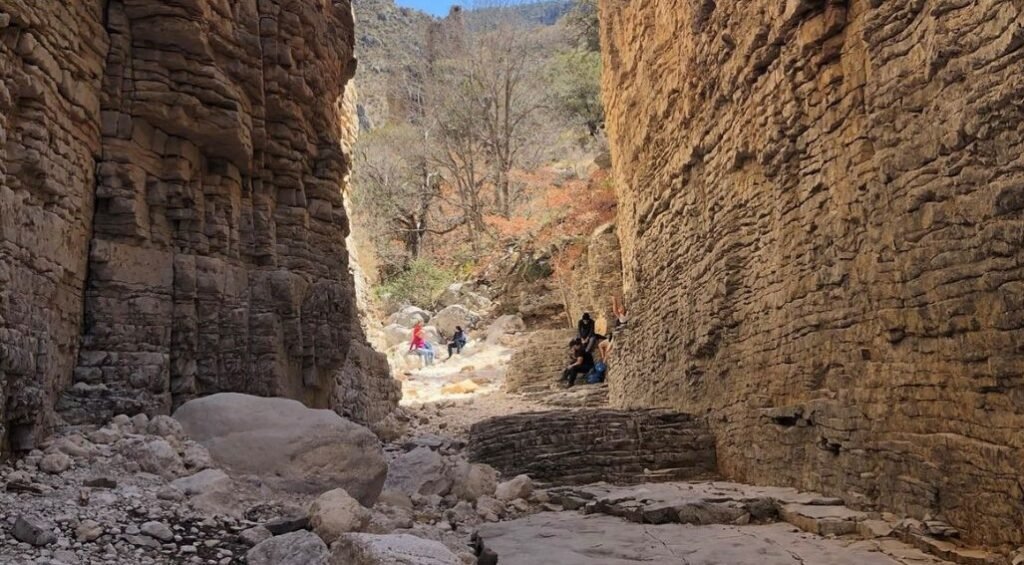 Groups of people standing in sunlight at the end of the tall, narrow canyon on the Devil’s Hall trail in Guadalupe Mountains National Park.