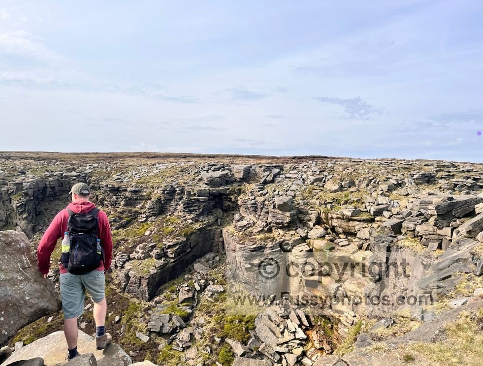 Person standing on the approach to Kinder Downfall, admiring the northern cliff where the valley drops steeply away out of sight.
