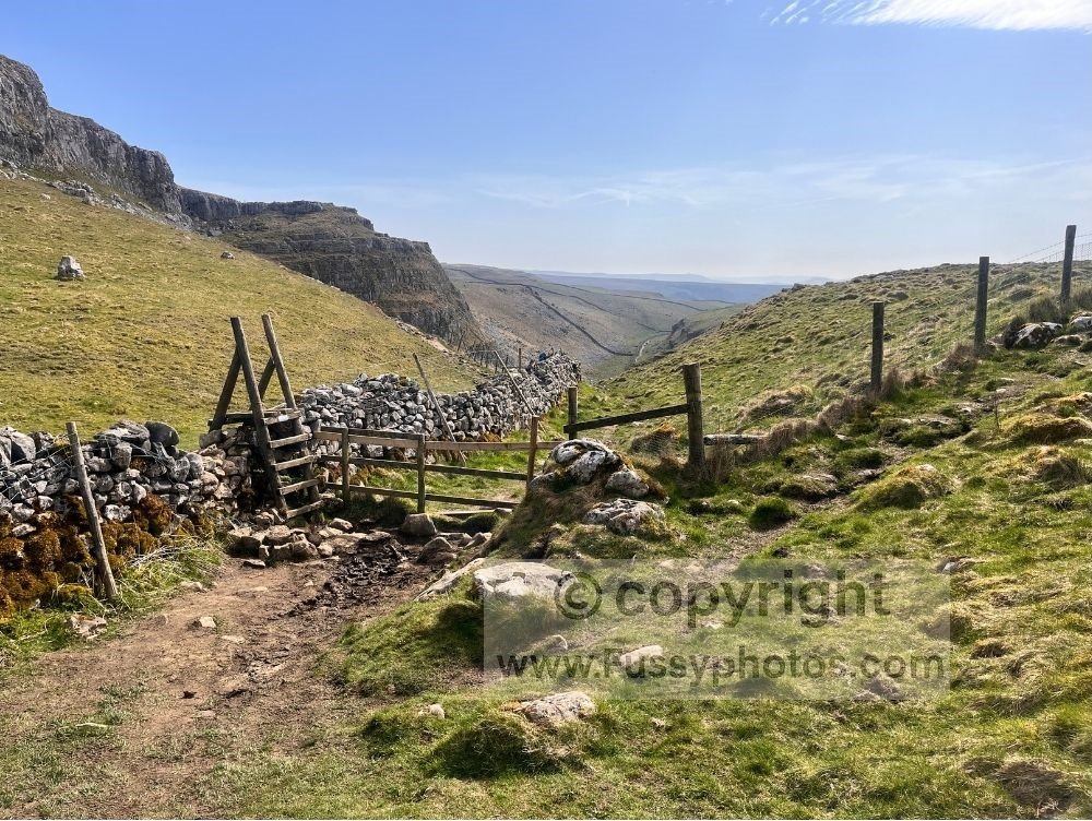 Ladder stile on the Pennine Way with a clear south‑facing view through Ing Scar towards the limestone pavement at Malham Cove.