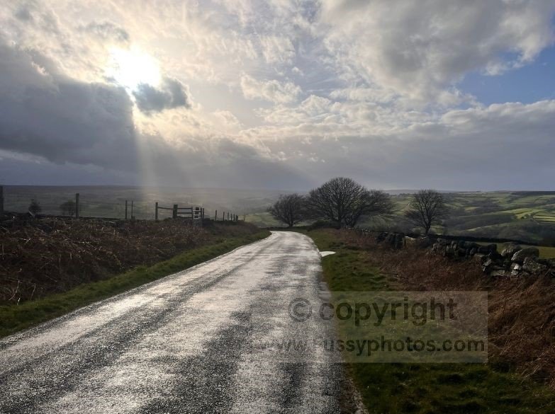 View west from Sleights Moor after the storm, with bright sunlight cutting through the clouds and illuminating the hills and the village of Grosmont in the distance.