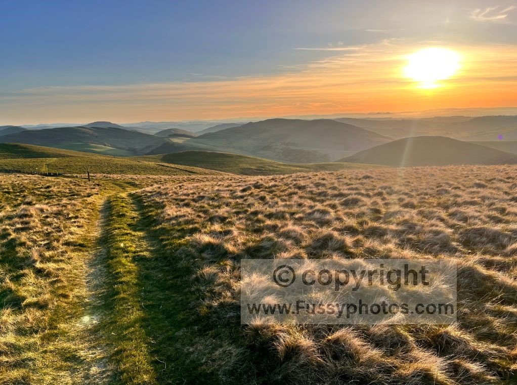 Sunset over the Cheviots, looking west towards Kirk Yetholm, with empty hills and warm evening light.
