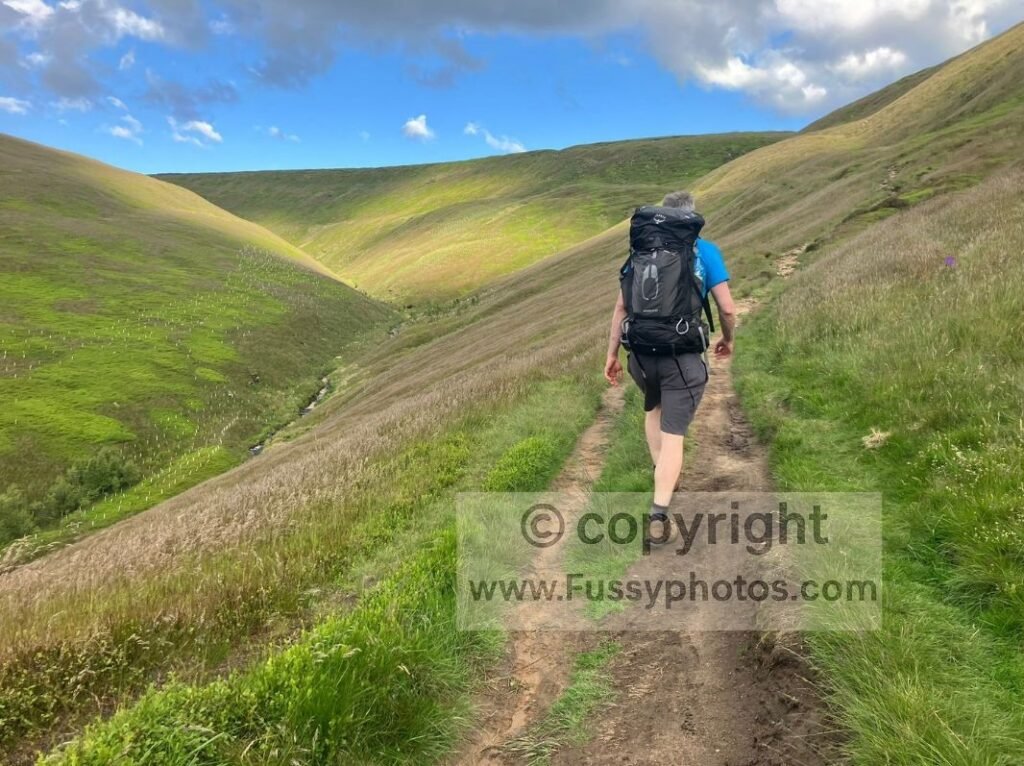 Walker carrying a fully loaded 65L backpack on a day hike, testing kit before long Pennine Way stages.