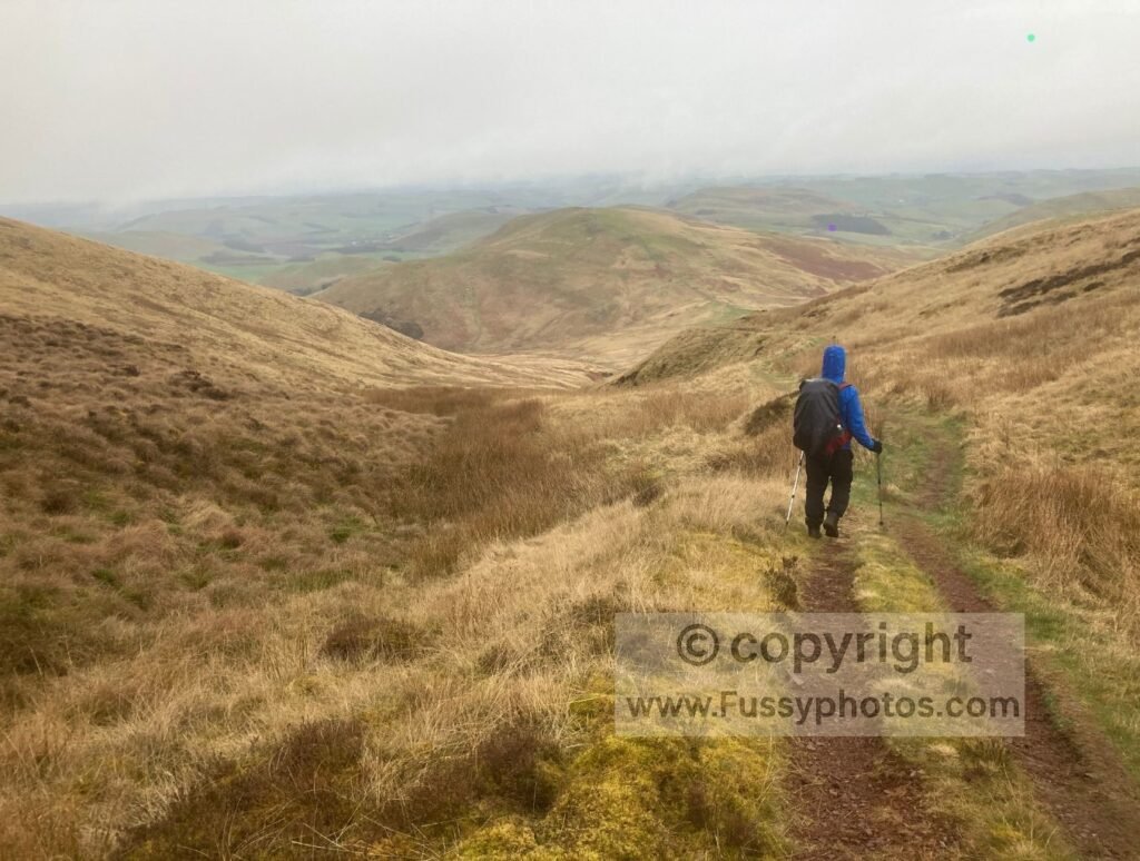 Friend descending the low‑level Pennine Way route with low cloud above the valley.