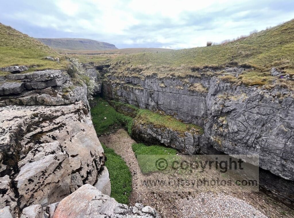 Hull Pot with Pen‑y‑Ghent in the background, showing the collapsed cavern and surrounding limestone.