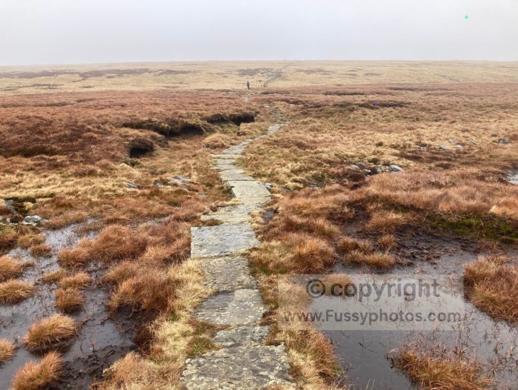 Stone slabs crossing high moorland towards Great Shunner Fell, showing a long, exposed stretch of the Pennine Way.