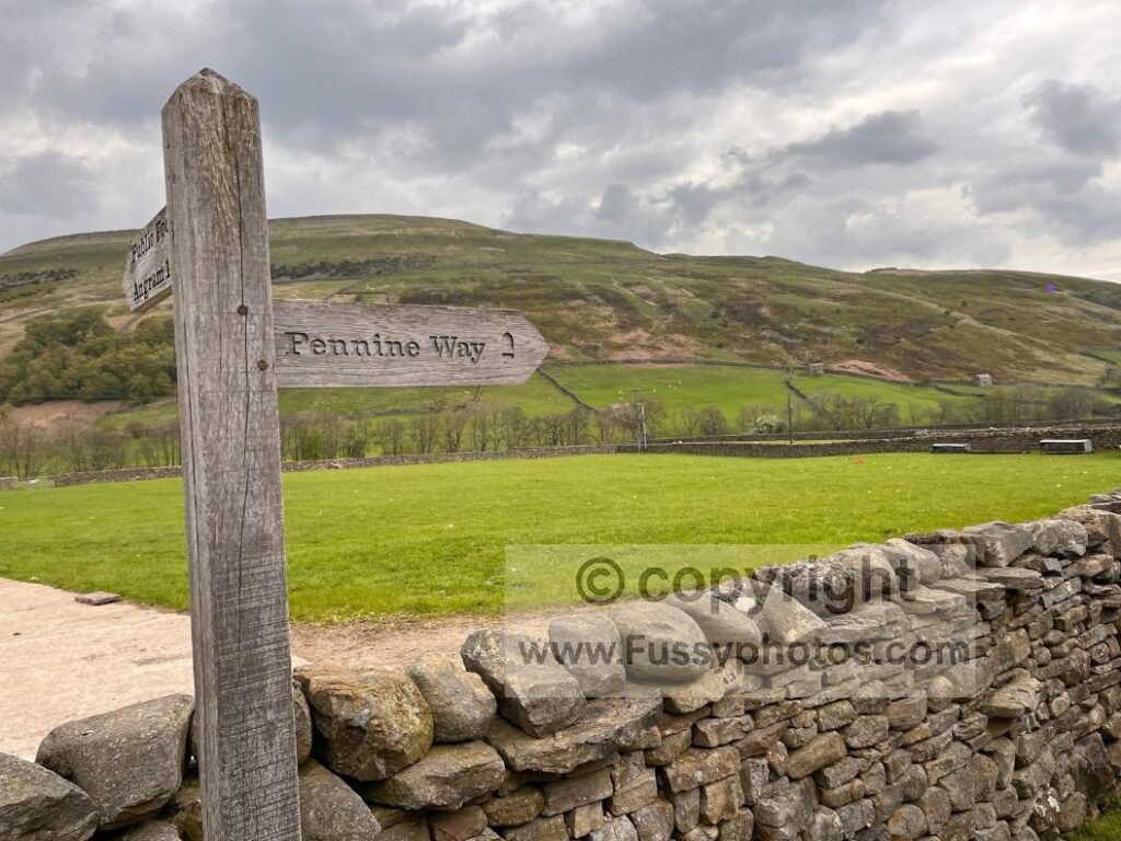 Pennine Way waymark in Thwaite at the junction where the trail turns sharply uphill.