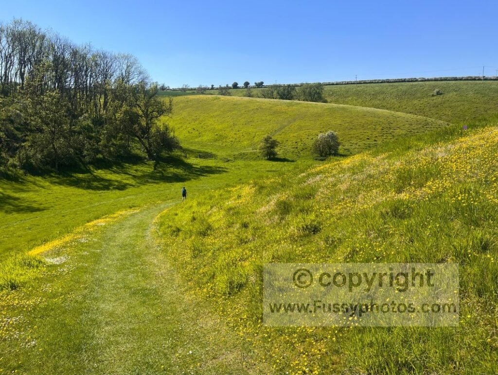 Walker heading down the slope into the centre of Brubber Dale on the Wolds Way, with the dry valley widening ahead and the soft contours becoming more defined.