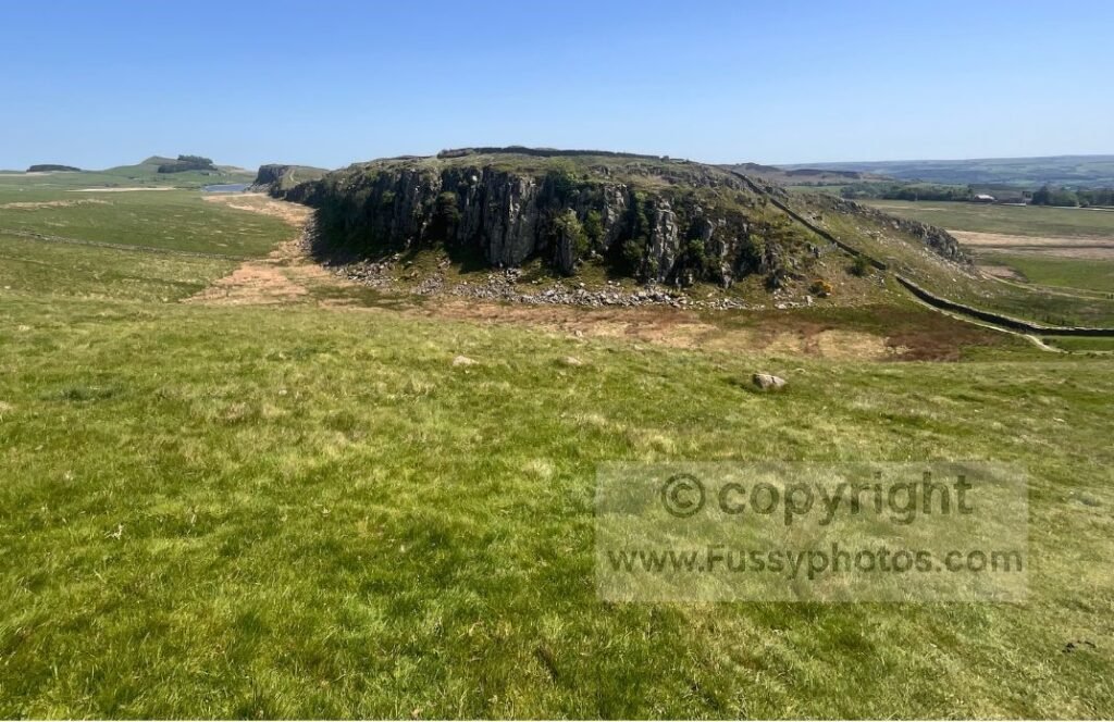 Steel Rigg crag with distant Crag Lough — Photo showing the huge crag of Steel Rigg rising sharply, with Crag Lough just visible to the left in the distance.