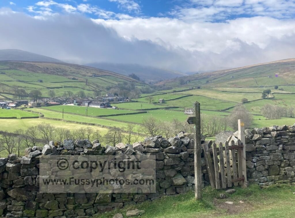 Elevated view of Thwaite and Swaledale, showing dry‑stone walls and farm buildings as the Pennine Way climbs back uphill after Great Shunner Fell.