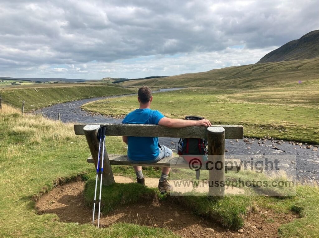 Wide meander of the River Tees with a bench and a person seated, viewed from the Pennine Way as the valley begins to narrow.
