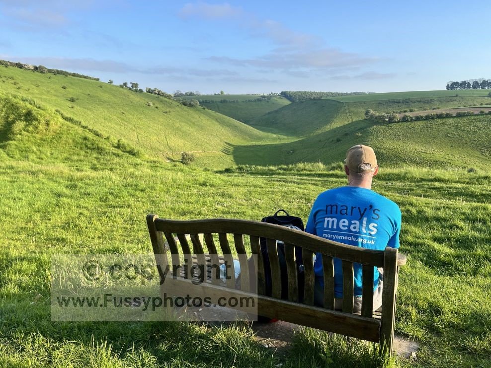 Person sitting on a bench above Thixen Dale, looking across the steep chalk sides and grassy valley floor that define the Wolds Way dry‑valley landscape.