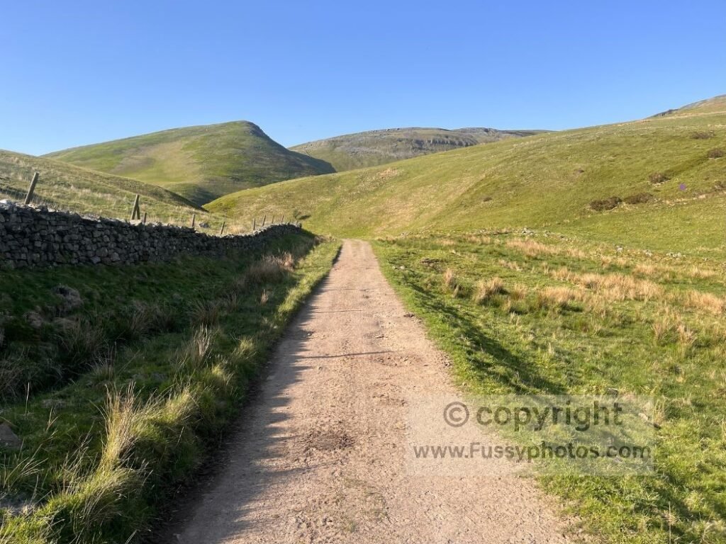 Great Rundale track alt text — Photo of the gravel farm track rising towards Great Rundale, with the valley partly obscured by interlocking spurs.