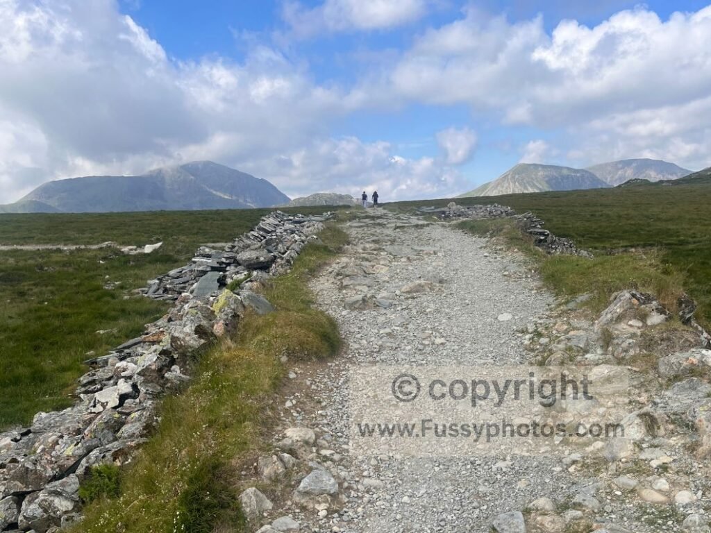 Flattened section of the Coast to Coast near Drum House, showing the trail junction and the peaks of Haystacks and High Crag on the horizon.