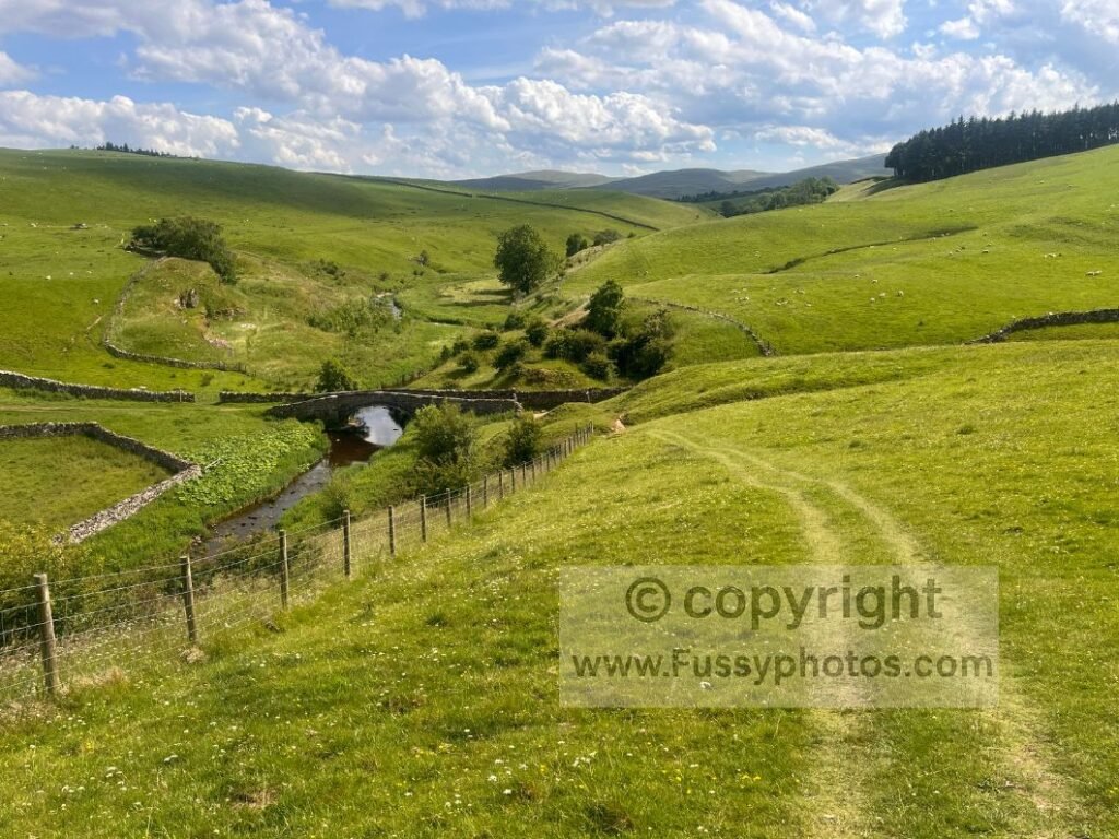 Arched stone Smardale Bridge crossing Scandal Beck, surrounded by rolling green hills on the C2C route.