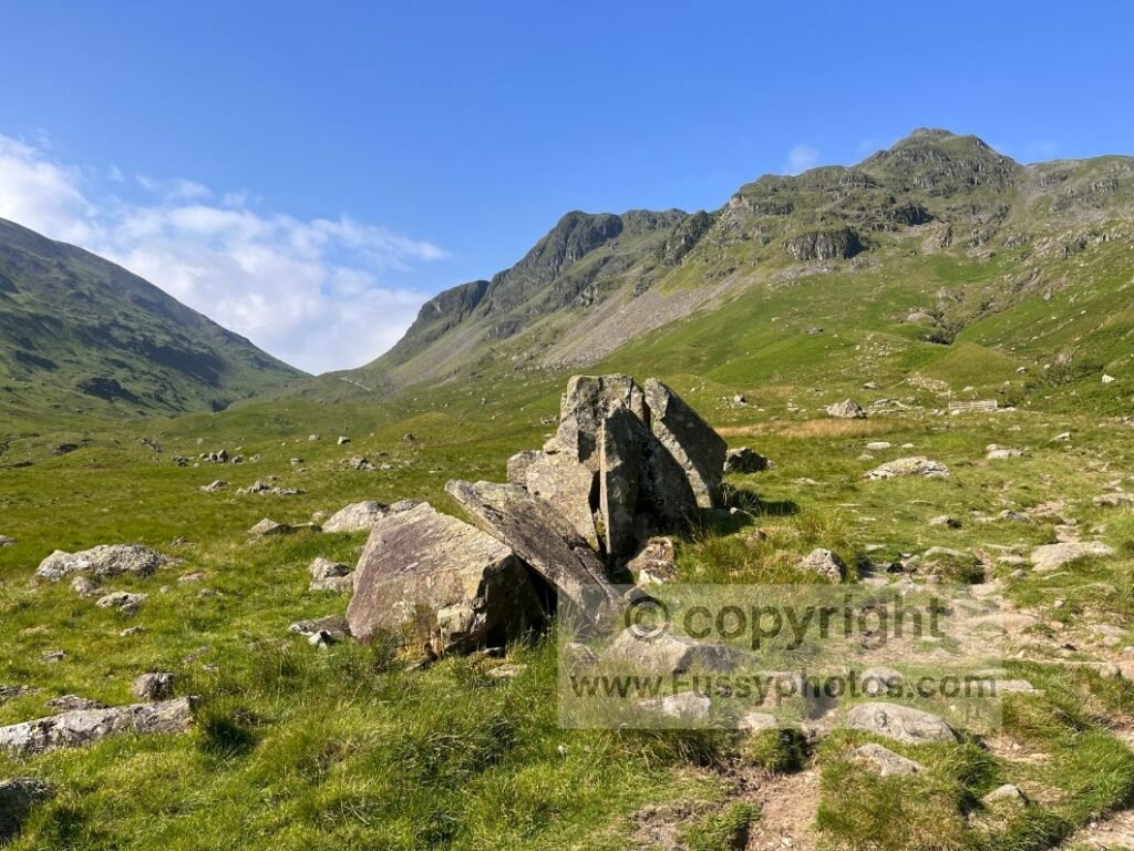 Glacial erratics beside the Coast to Coast trail in Grisedale Valley with waterfall on valley side.