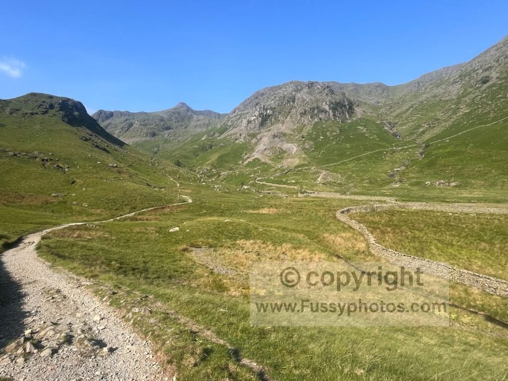 Blue‑sky view across Grisedale Valley with wide glaciated slopes and the Coast to Coast track ahead.