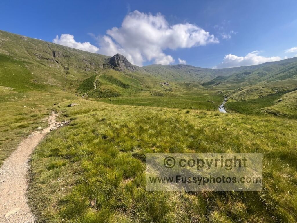 Steep crag behind with amphitheatre and U‑shaped valley visible ahead.