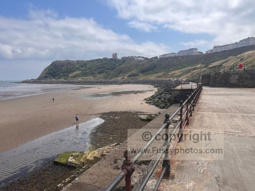 View of the rock armour and curved sea wall at the south end of Scarborough North Bay, leading towards the steep cliffs of Castle Cliff on the Cleveland Way.