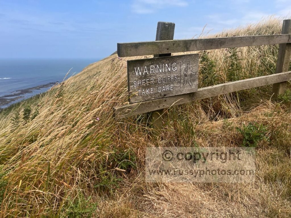 “Sheer Cliffs” sign near the holiday park on Gristhorpe Cliff, overlooking Castle Rocks and Gristhorpe Sands along the Cleveland Way.