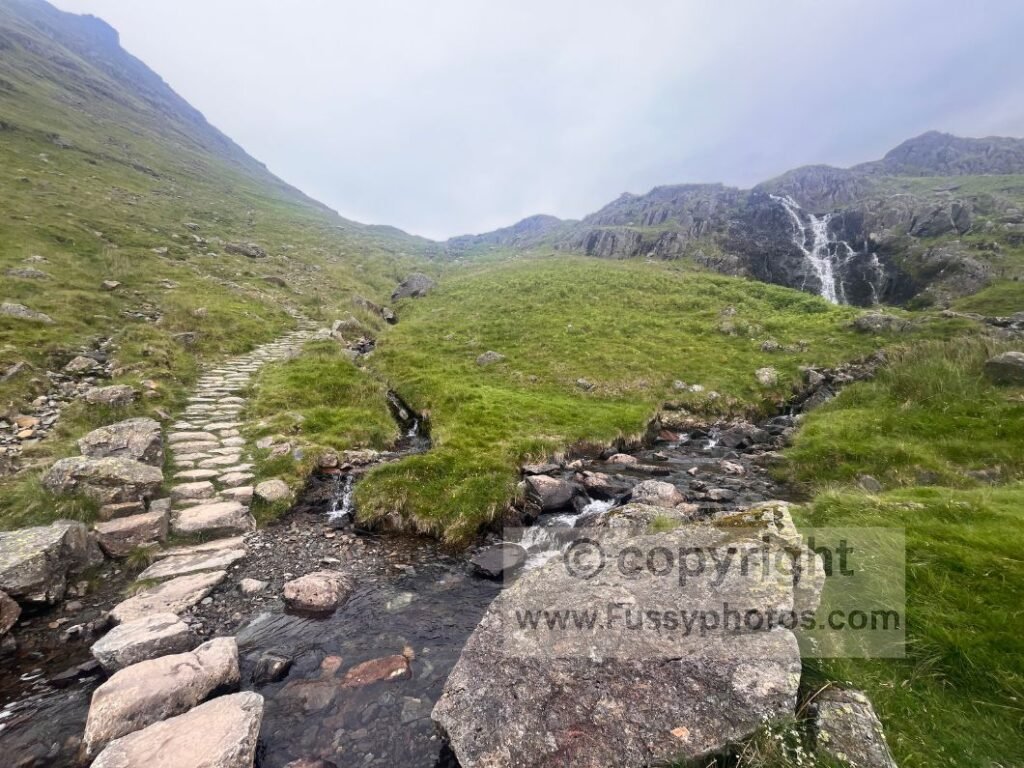 Small waterfall on beck descending into Grasmere with valley opening below.