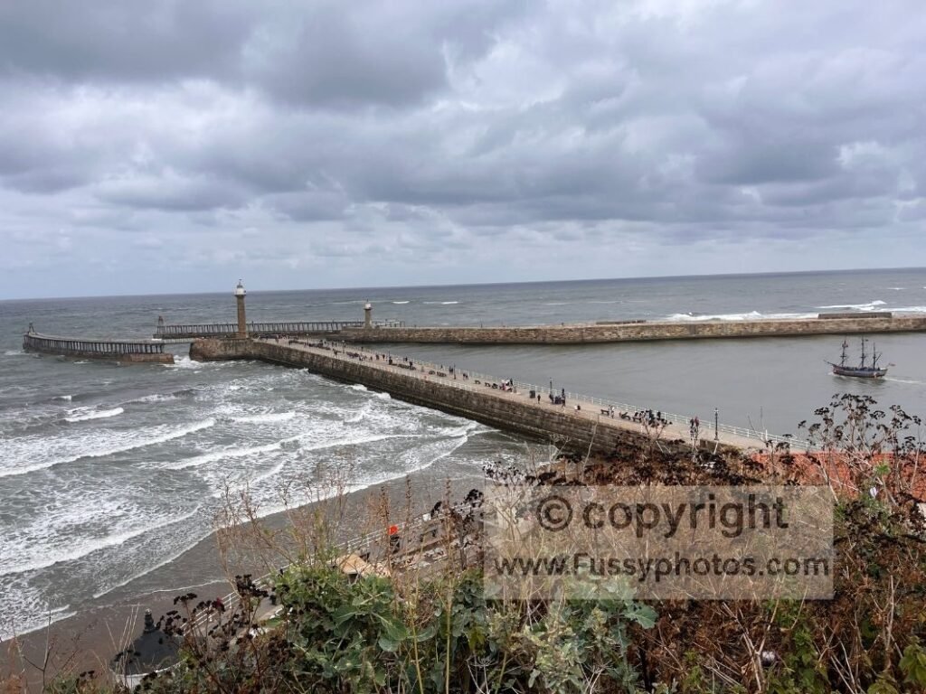 The Black Pearl boat sailing out of Whitby Harbour towards the sea, photographed from the Cleveland Way approach.