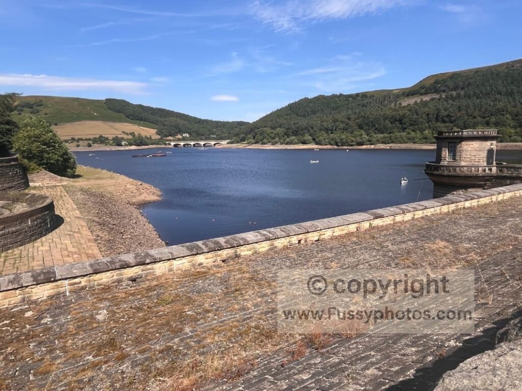 Low water levels at Ladybower Reservoir with the bellmouth overflow visible on the left; exposed reservoir banks and calm water beneath Win Hill on the short circular route.