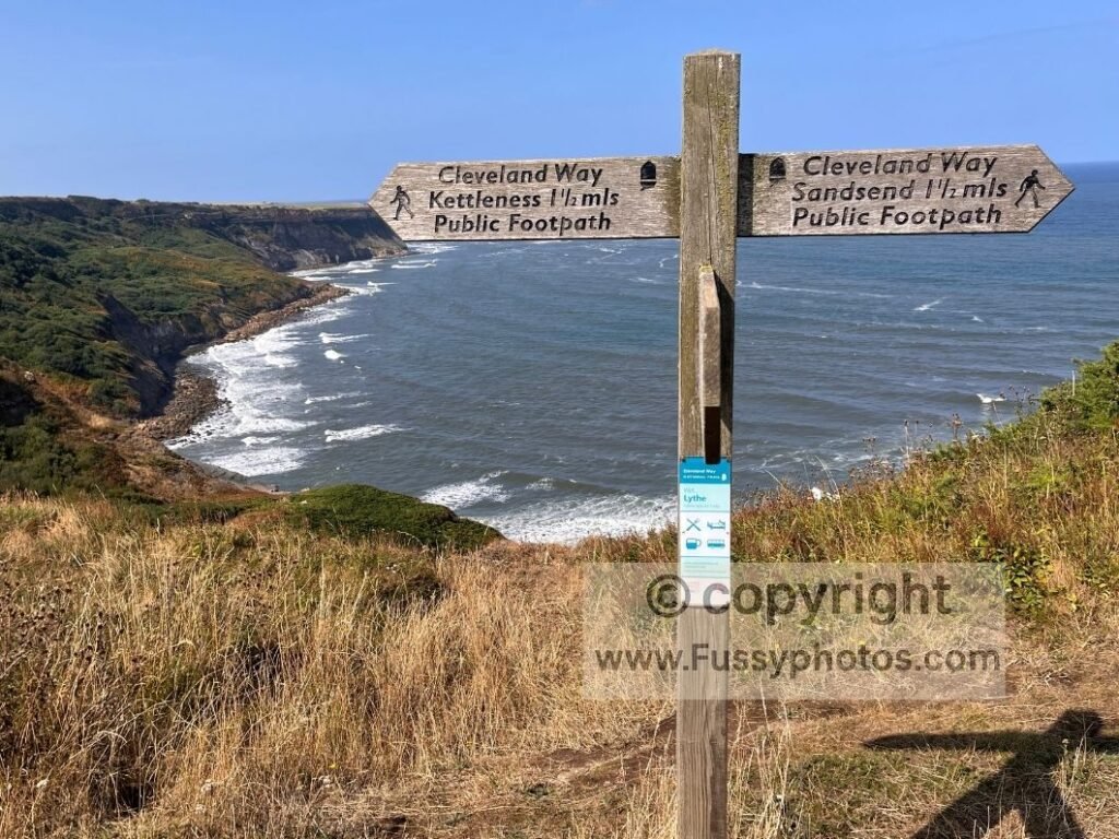 Trail sign on the Cleveland Way with north‑facing views towards Ovalgate Cliff above the coastline.