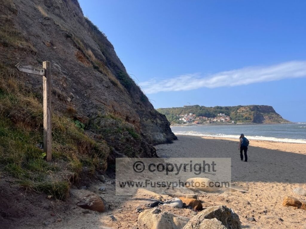 Trail sign on Runswick Sands with cliffs and beach ahead, photographed from the shoreline while walking west.