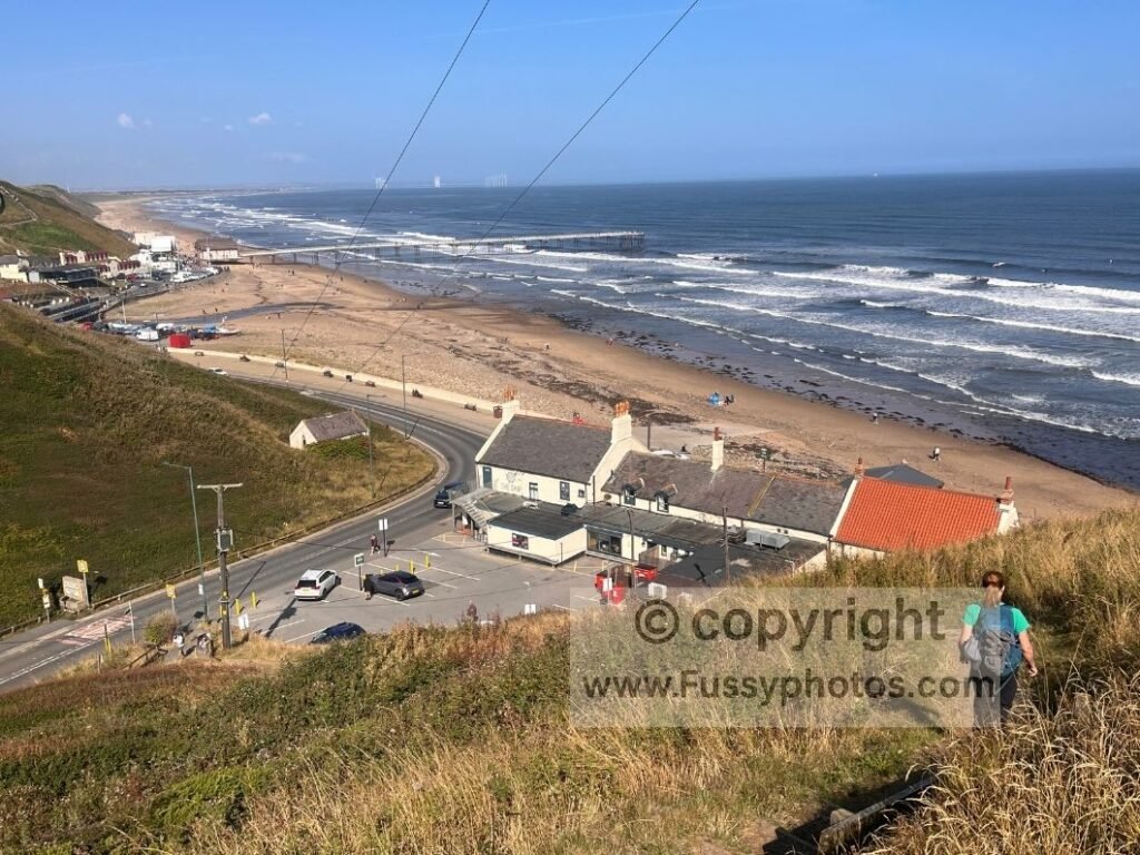 Looking down the steep steps towards Saltburn‑by‑the‑Sea, showing The Ship Inn at the base of the descent and the sweeping beach and pier beyond Saltburn Sands.